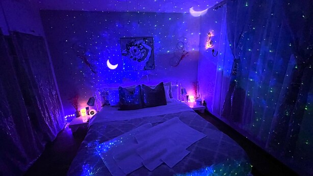Une chambre à coucher avec un lit, des oreillers, une table de chevet, une horloge murale et une décoration en forme de croissant de lune.