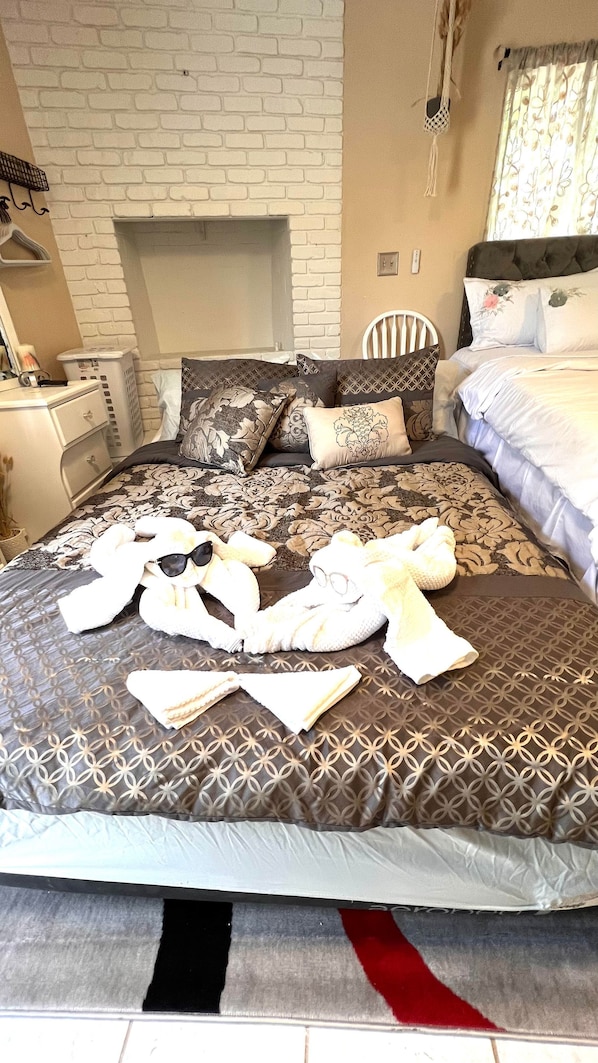 A neatly made bed with floral bedding, a white brick wall, and a small white chair.