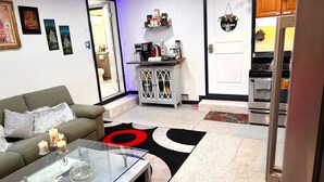 Un salon avec un canapé, une table basse en verre et un tapis rouge et noir. Il y a également un coin cuisine équipé d’un réfrigérateur, d’un four et d’une machine à café.