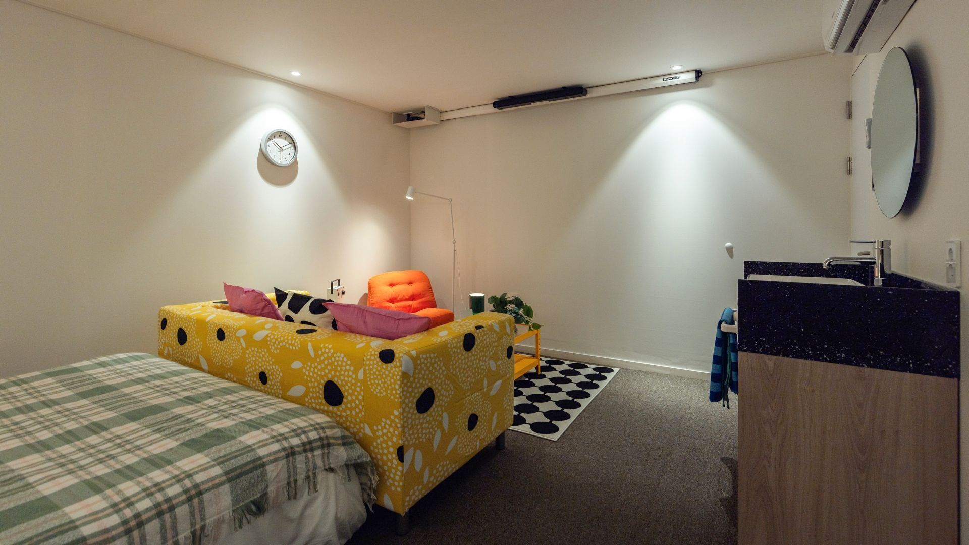 Una habitación compacta con dos camas, una mesita de noche, un espejo y un baño pequeño con lavamanos y espejo.