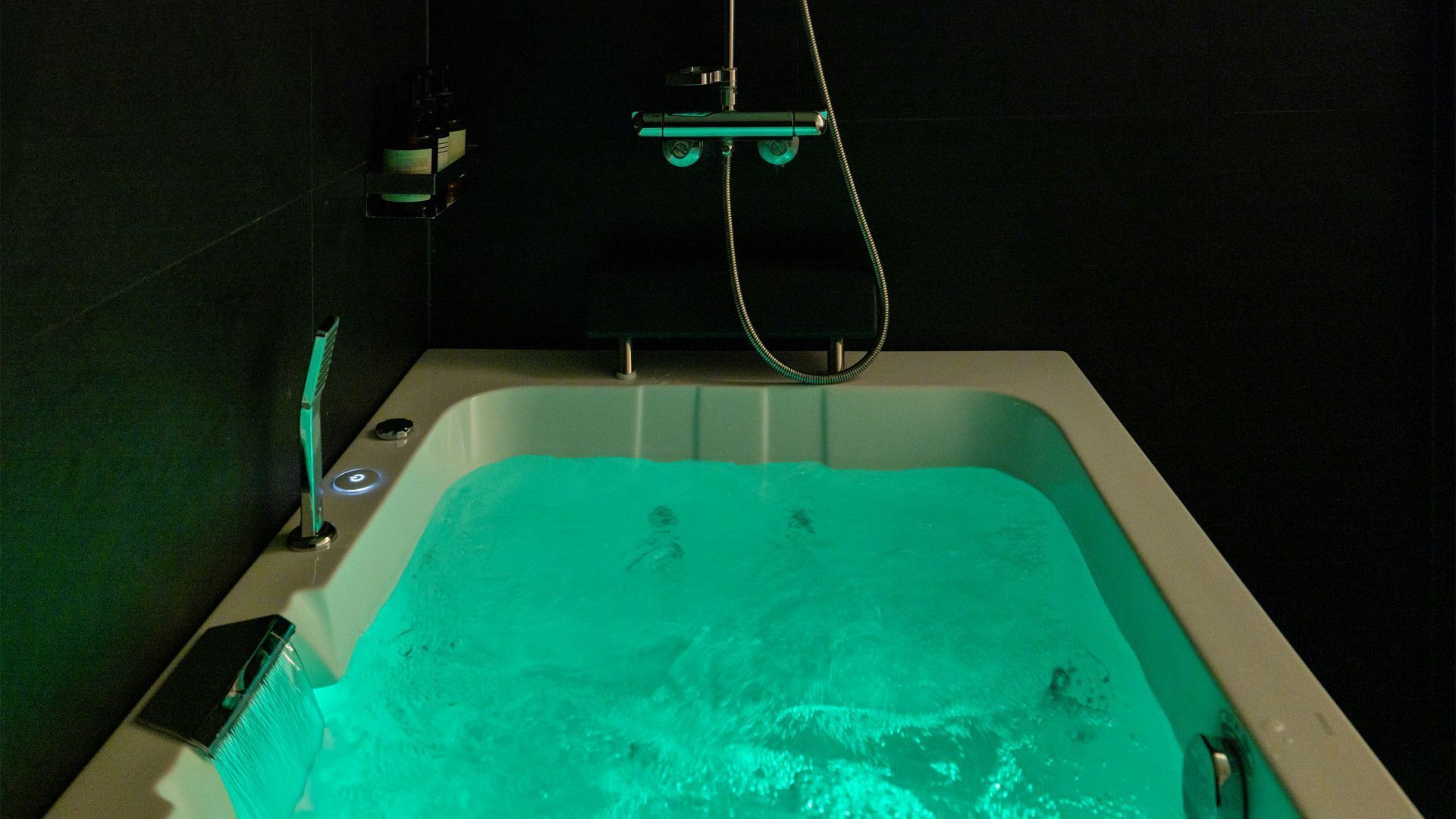 Vihreällä valolla varustettu kylpyamme, käsisuihku ja pullo shampoota.
