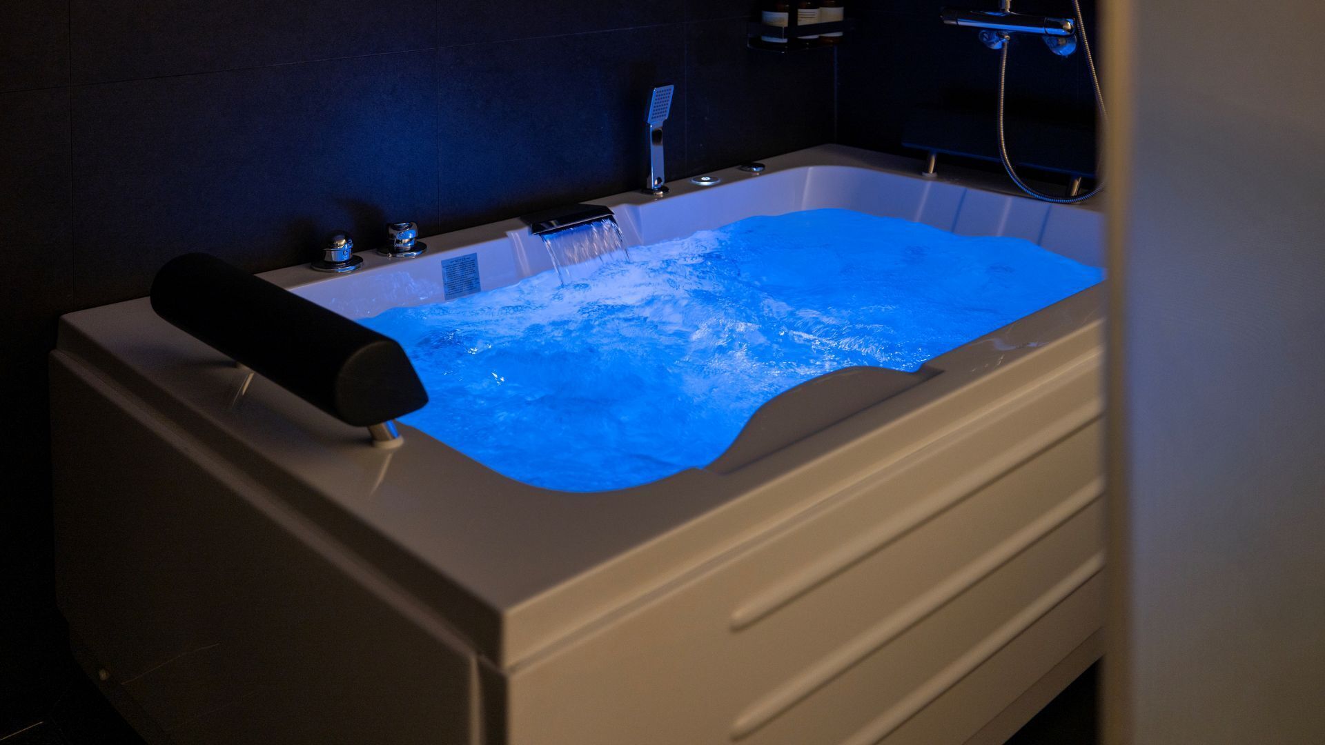 A bathtub with a blue light feature, a handheld showerhead, and a control panel.