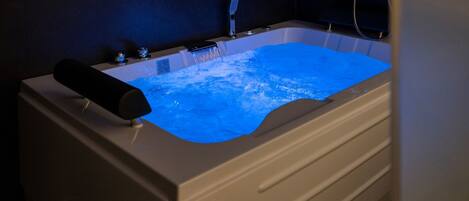 A bathtub with a blue light feature, a handheld showerhead, and a control panel.