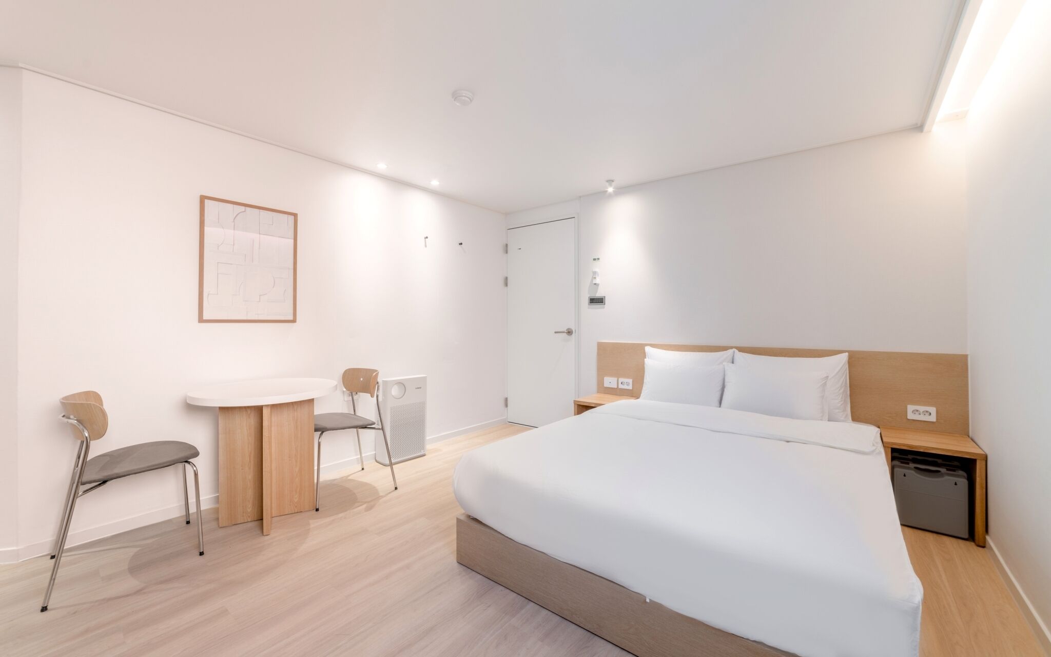 A modern hotel room with a large bed, a small desk, a chair, and a radiator.