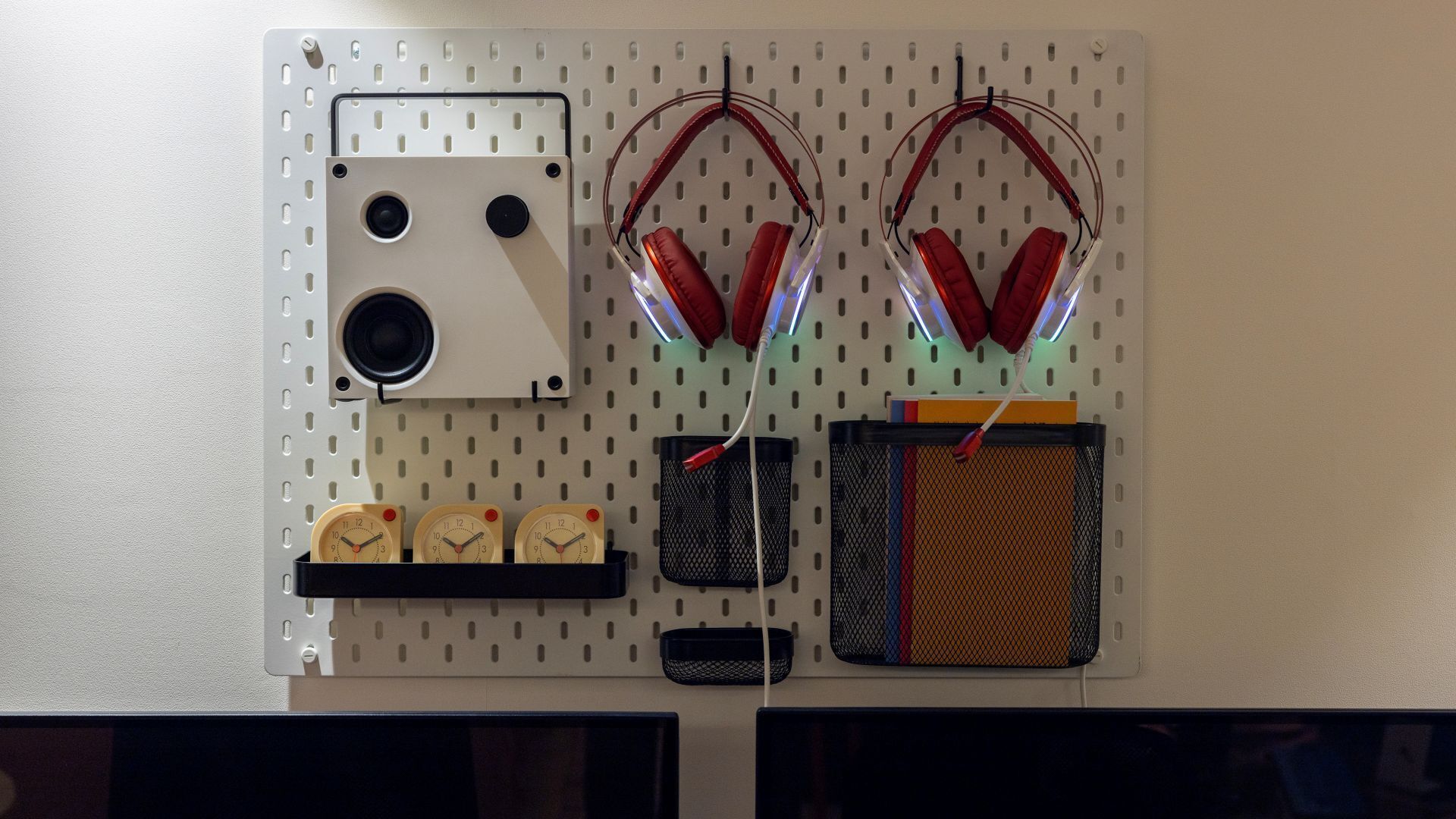 A pegboard wall with a white cassette player, red headphones, and three clocks.