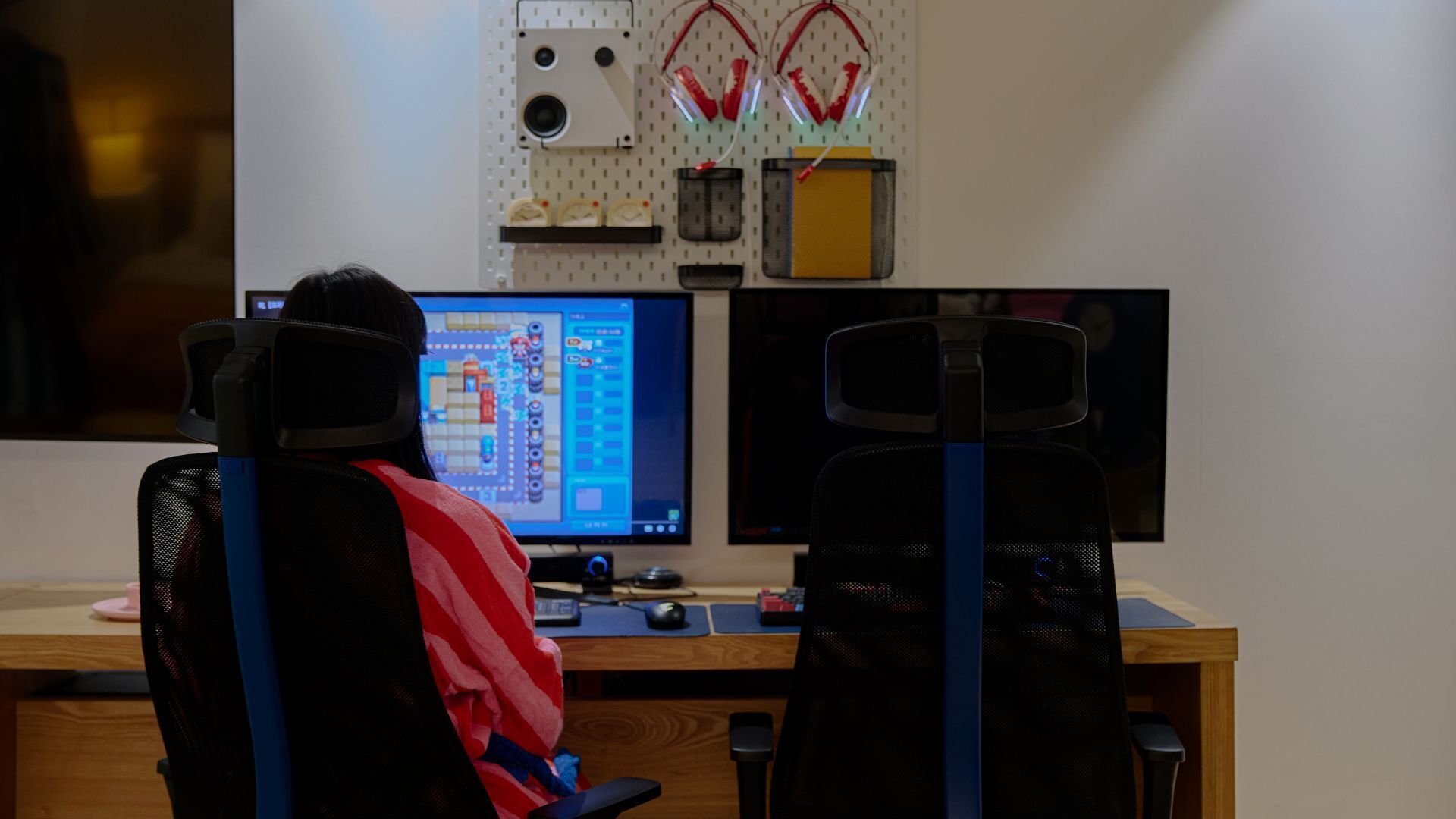 A person sitting at a desk with two monitors, headphones, and a keyboard.