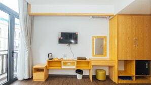 A hotel room with a wooden desk, a television mounted on the wall, a mirror, and a wardrobe. - MARUKO HOTEL HA LONG (Bai Chay)