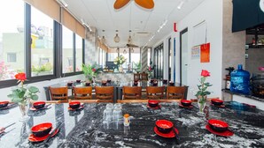 A restaurant with marble tables, red and black tableware, wooden chairs, and ceiling fans. - MARUKO HOTEL HA LONG (Bai Chay)