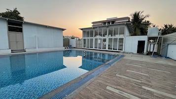 A swimming pool with a tiled deck, surrounded by buildings with large windows and a clear sky.