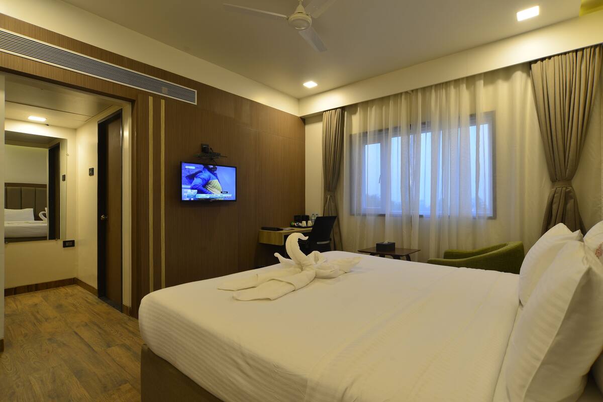 Ein Hotelzimmer mit Bett, Wandfernseher, Schreibtisch und einem Fenster mit Vorhängen.