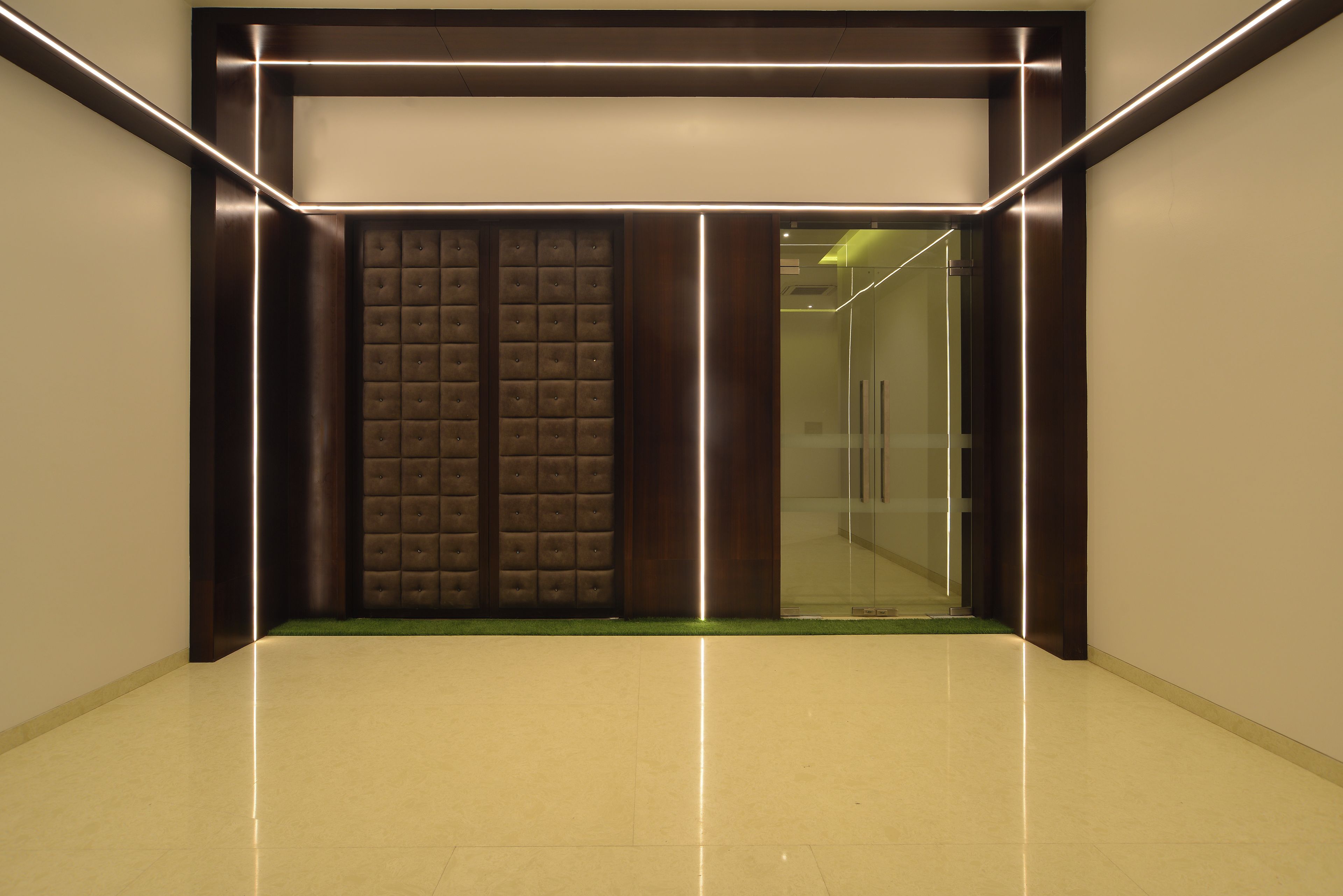 A modern elevator with a metallic finish and illuminated edges, leading to a glass door.