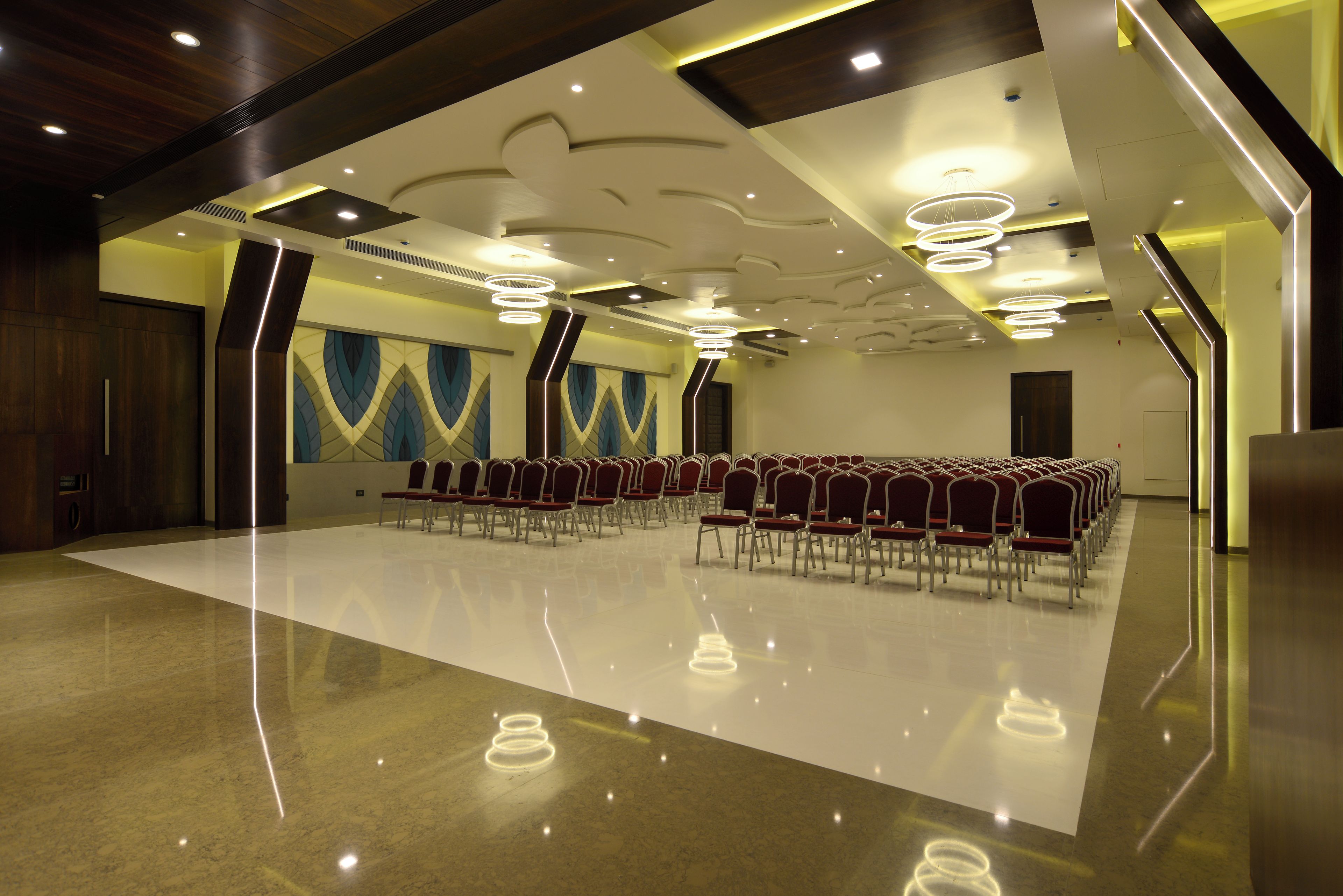 Un salón de conferencias con una hilera larga de sillas, piso pulido y un diseño moderno de techo con iluminación empotrada.