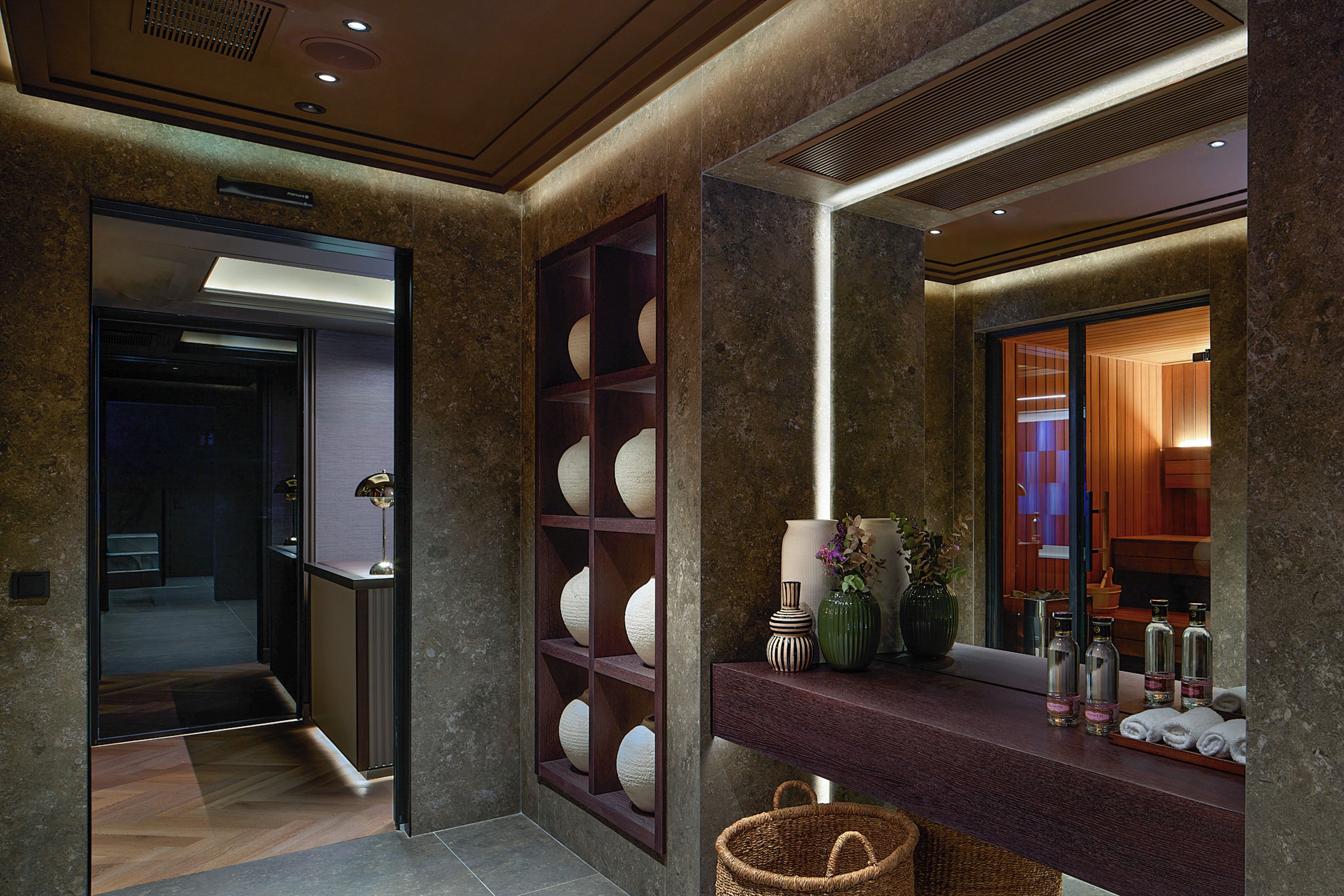 A modern bathroom with a marble wall, a vanity with a mirror, and a shelf with decorative items.