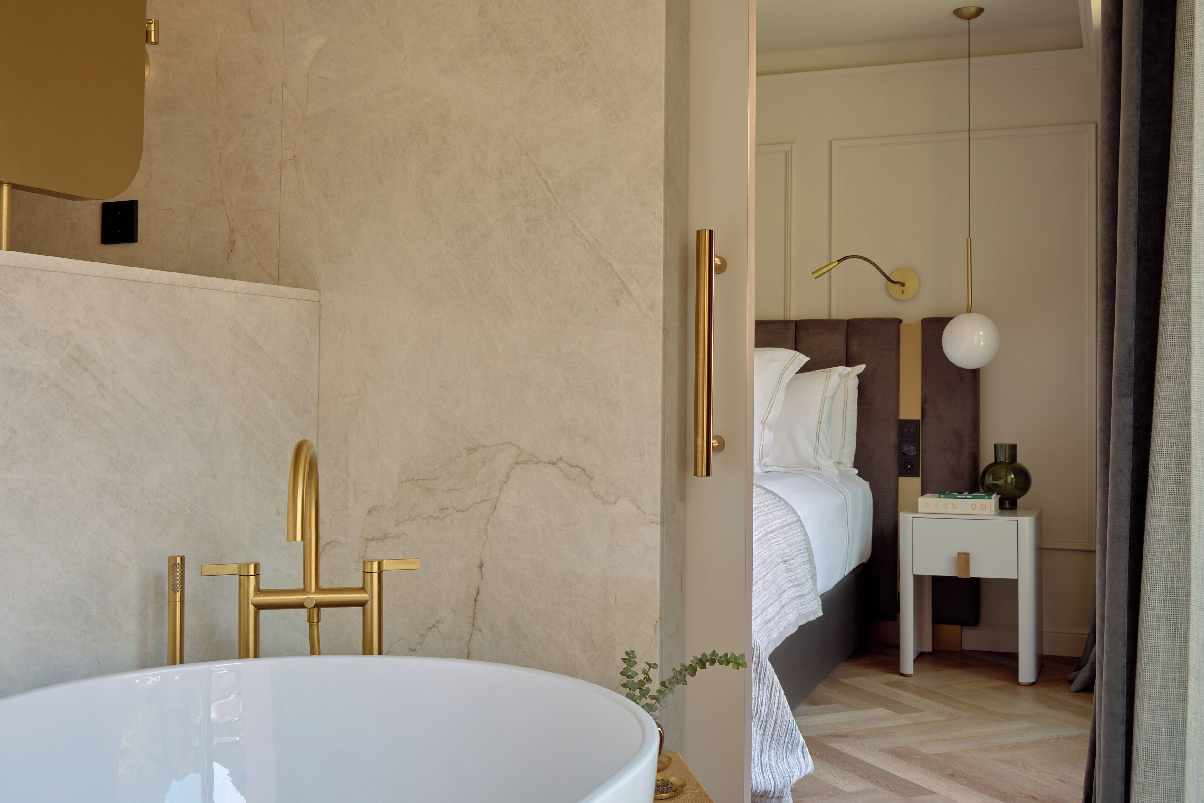 A modern bathroom with a large white bathtub, gold fixtures, and a marble wall.