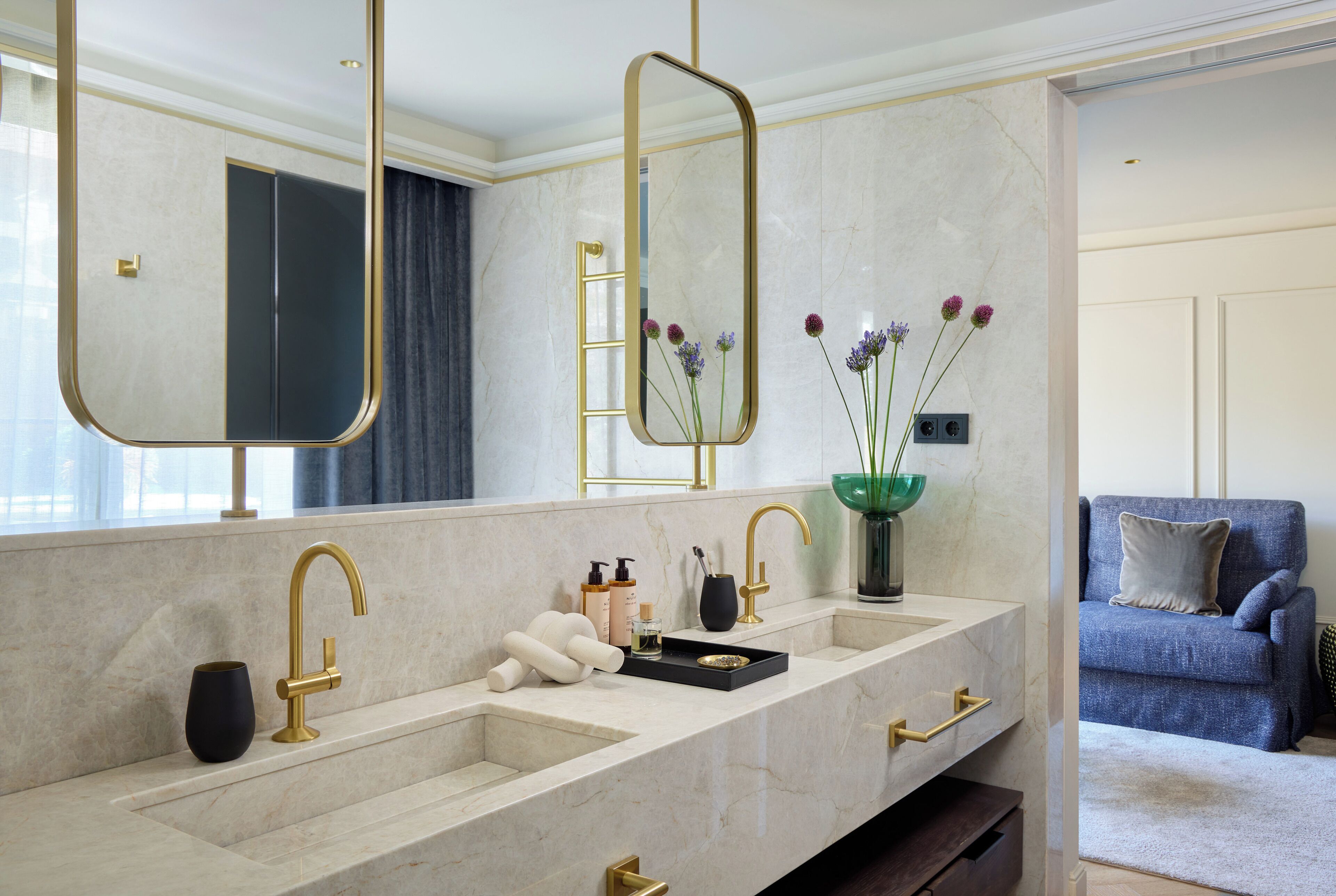 A modern bathroom with a dual sink, gold fixtures, and a large mirror.