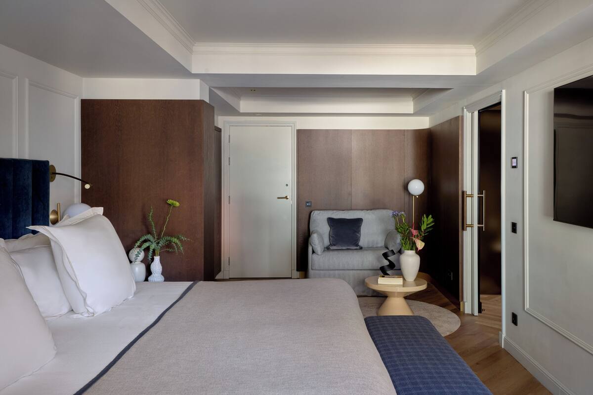 A hotel room with a large bed, a sofa, a small table with a lamp, and a TV.