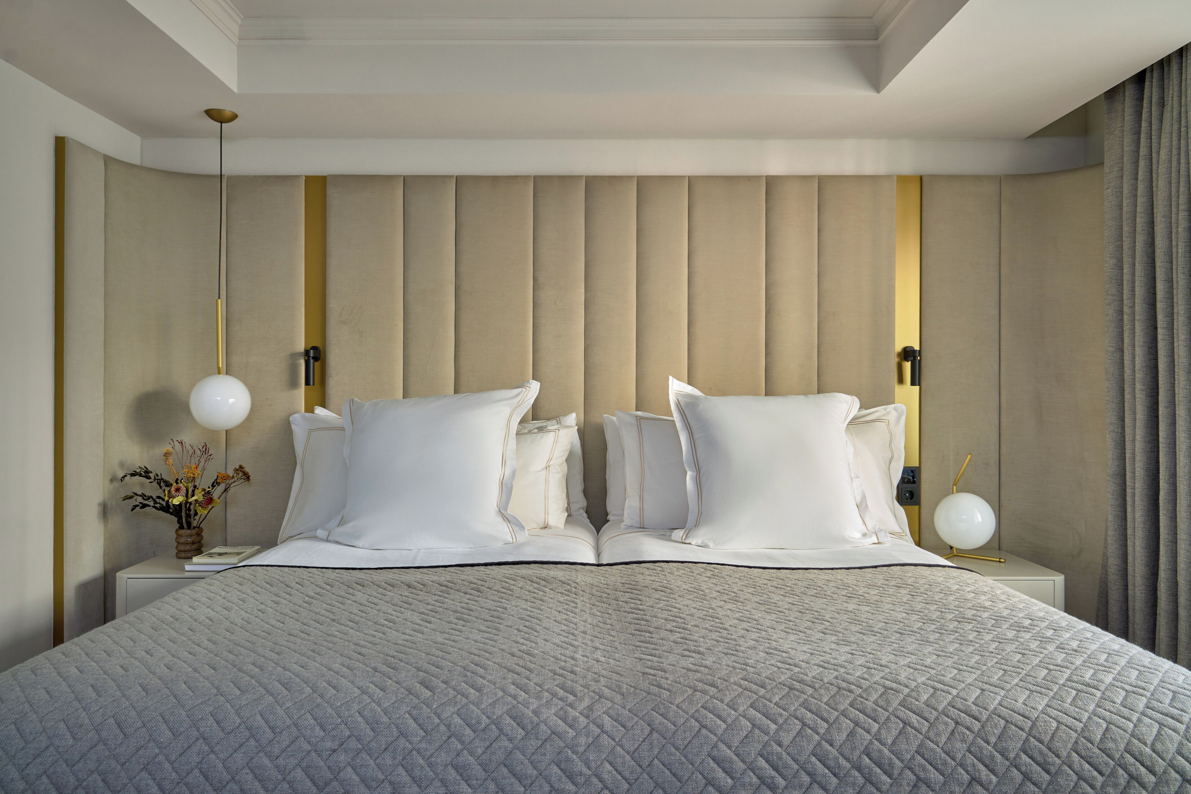 Una cama bien hecha con una colcha acolchada, dos mesitas de noche con lámparas, y una pared con paneles verticales.