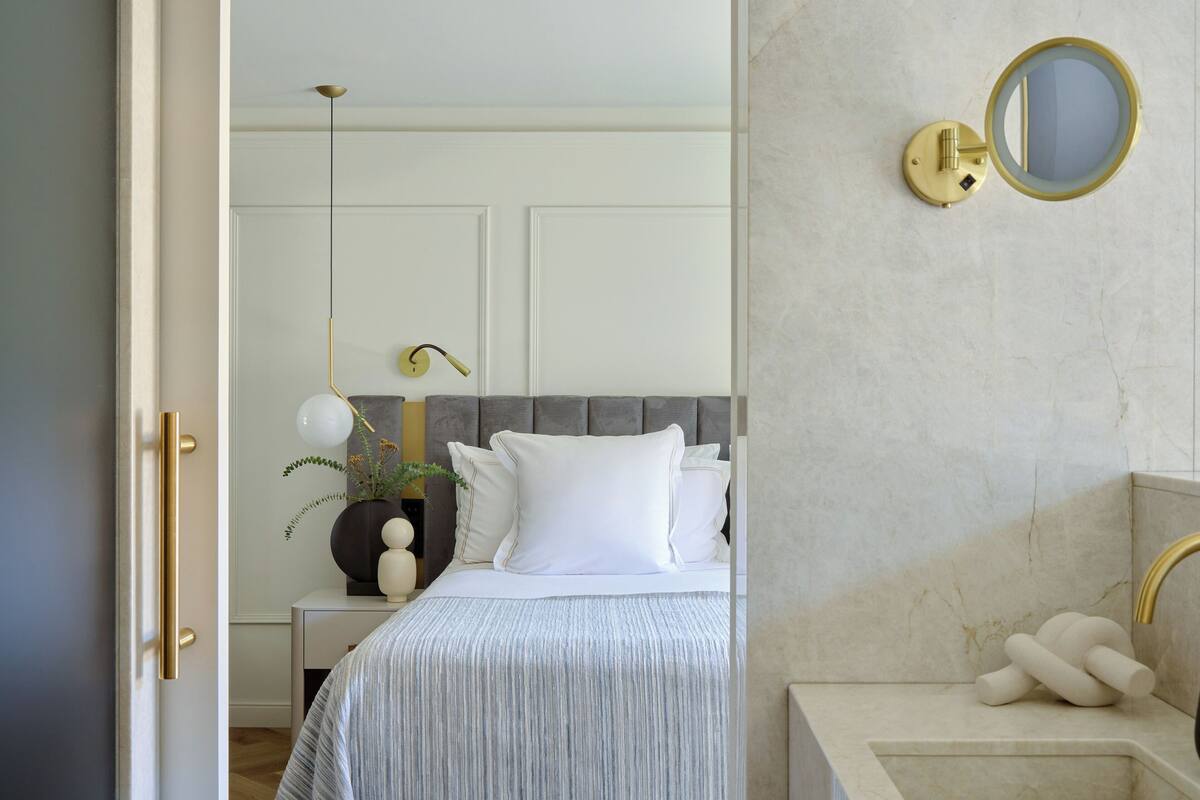 A bedroom with a bed, bedside table, lamp, and a wall-mounted mirror.