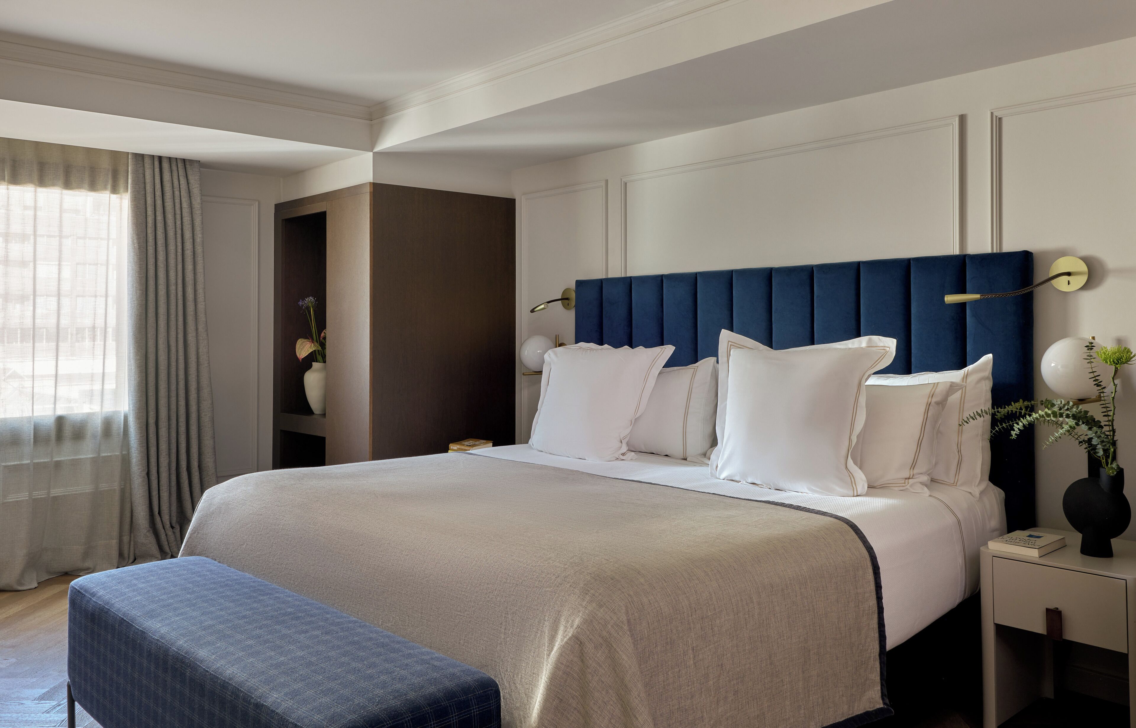 Une chambre d’hôtel bien rangée, avec un grand lit, une table de chevet avec une lampe et une fenêtre avec des rideaux.