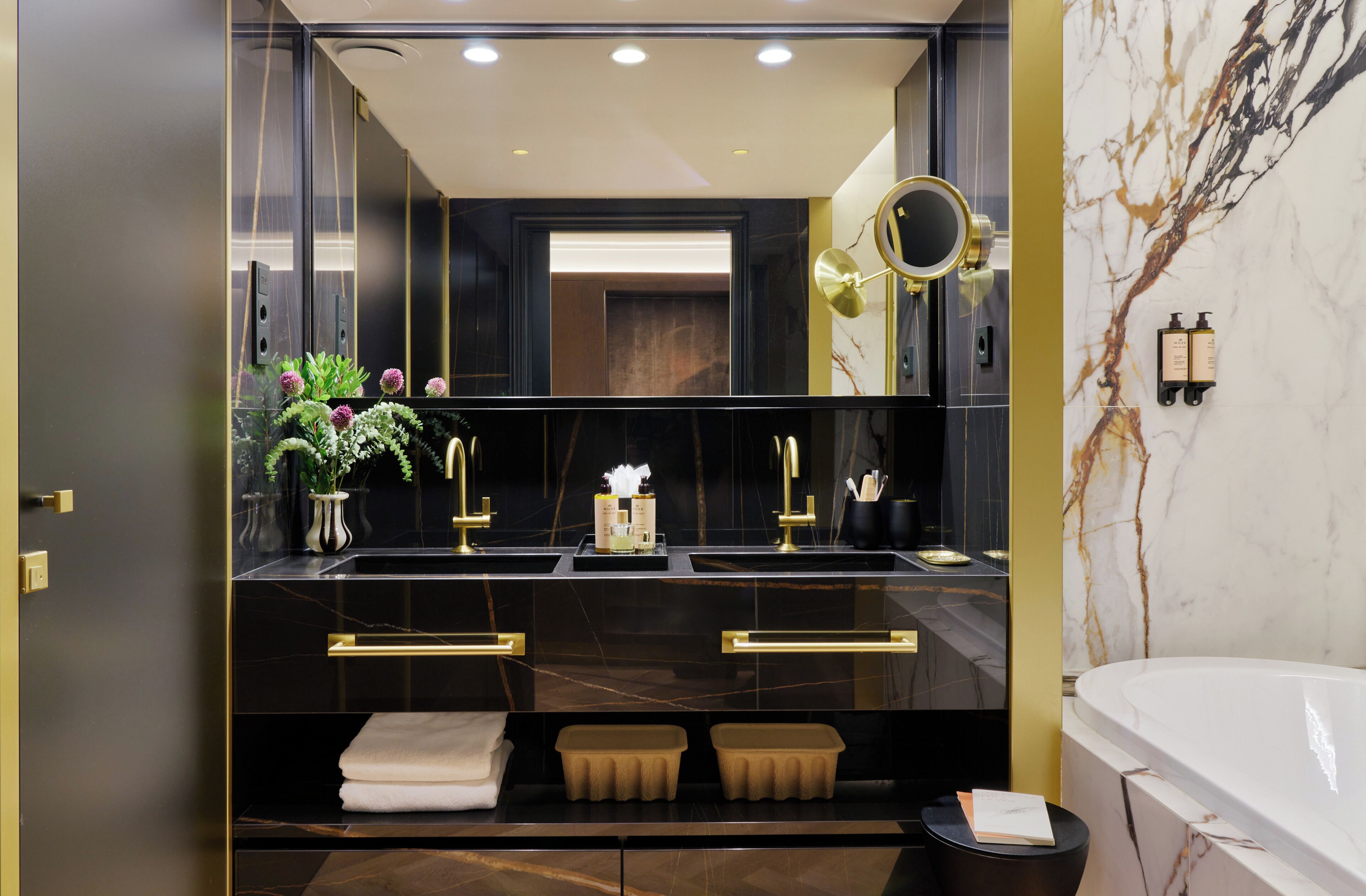 A modern bathroom with a double sink, a large mirror, a vanity with a marble countertop, and a bathtub.