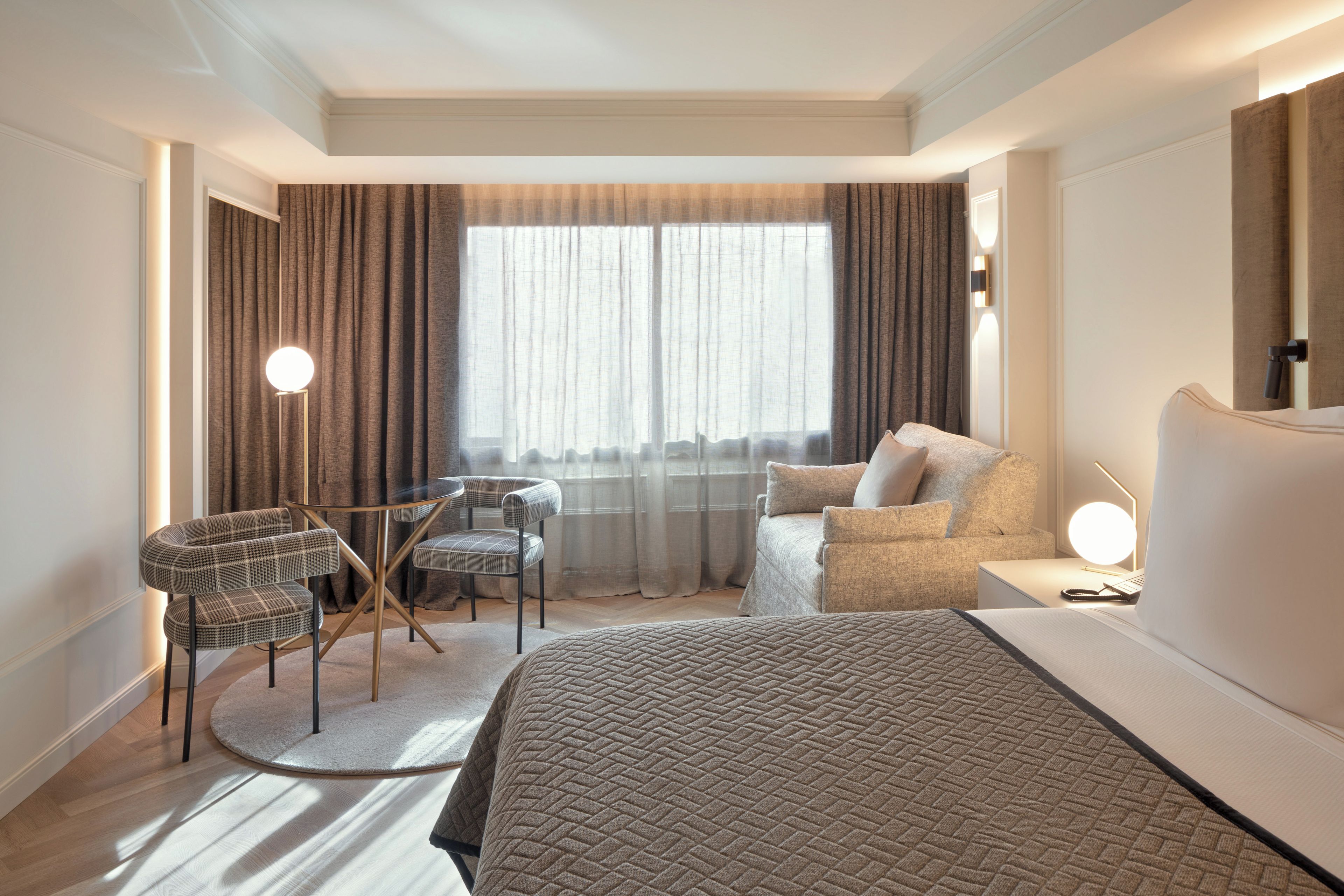 A hotel room with a bed, a desk, a chair, and a sofa.