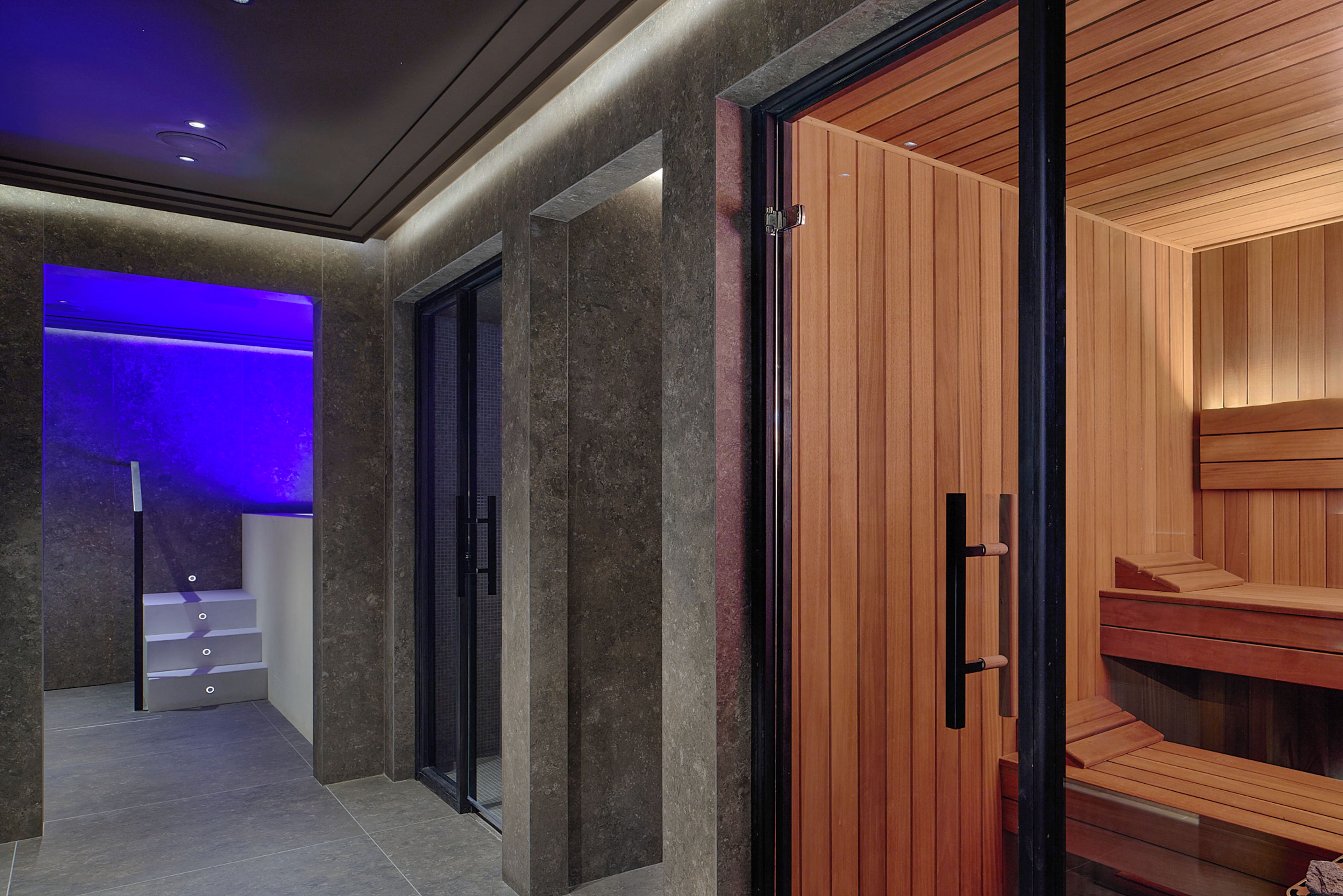 A modern interior with a sauna area, a glass door, and a blue-lit hallway.