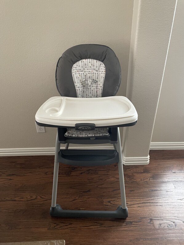 A high chair with a tray, positioned against a wall with a wooden floor. - New, beautiful 5 BR, 10 beds, near AT&T Stad,Joe Pool, Sixflag, and pet friendly (Grand Prairie)