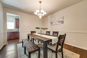 A dining area with a wooden table, chairs, a bench, a chandelier, and a painting on the wall.