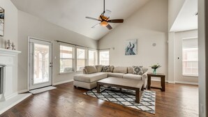 A spacious living room with a sectional sofa, hardwood flooring, a ceiling fan, and a fireplace. - New, beautiful 5 BR, 10 beds, near AT&T Stad,Joe Pool, Sixflag, and pet friendly (Grand Prairie)