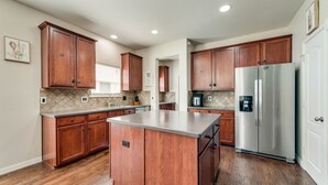 A modern kitchen with wooden cabinets, a stainless steel refrigerator, and a central island. - New, beautiful 5 BR, 10 beds, near AT&T Stad,Joe Pool, Sixflag, and pet friendly (Grand Prairie)