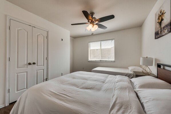 Une chambre à coucher avec un lit, un ventilateur de plafond, une fenêtre et une table de chevet avec une lampe.