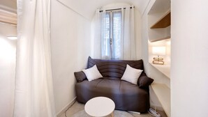 A small, cozy room with a brown sofa, a round table, and a window with sheer curtains.