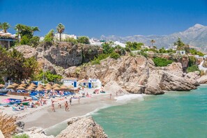 A beach with rocky cliffs, clear turquoise water, and a row of beach umbrellas.