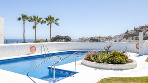 Ein Swimmingpool mit Blick auf das Meer, Palmen und ein weißes Gebäude.