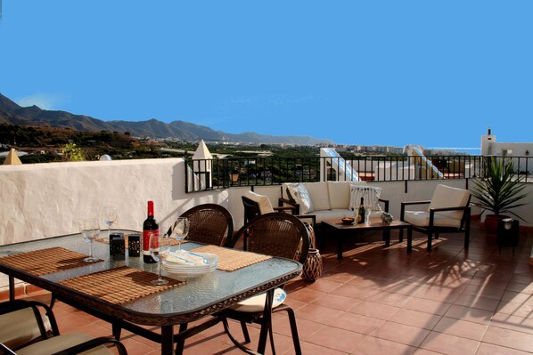 Une terrasse avec une table dressée pour le repas, des chaises, un canapé et une vue sur le paysage.