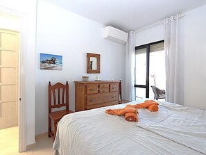 A bedroom with a bed, a wooden dresser, a chair, a painting, and a window with curtains.