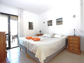 Une chambre à coucher comprenant un lit, une table de chevet, une commode et une porte-fenêtre coulissante donnant sur un balcon.
