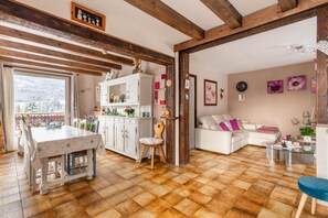 Un grand espace de vie comprenant un coin repas avec une table, un canapé blanc et une cuisine équipée de placards et d’une fenêtre.