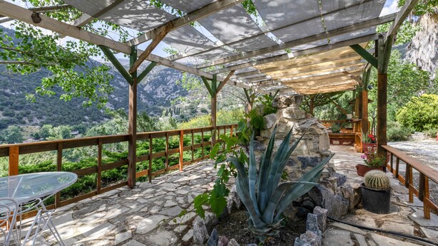 A covered patio with stone flooring, a table and chairs, and a view of a mountainous landscape.