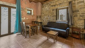 A rustic room with a stone wall, a wooden ceiling, a leather sofa, a dining table with chairs, and a small wooden table.