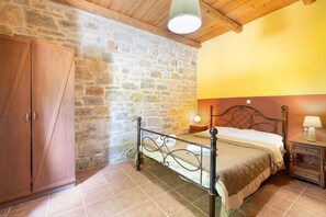 Une chambre avec un mur en pierre, un plafond en bois, un lit, une table de chevet et une armoire.