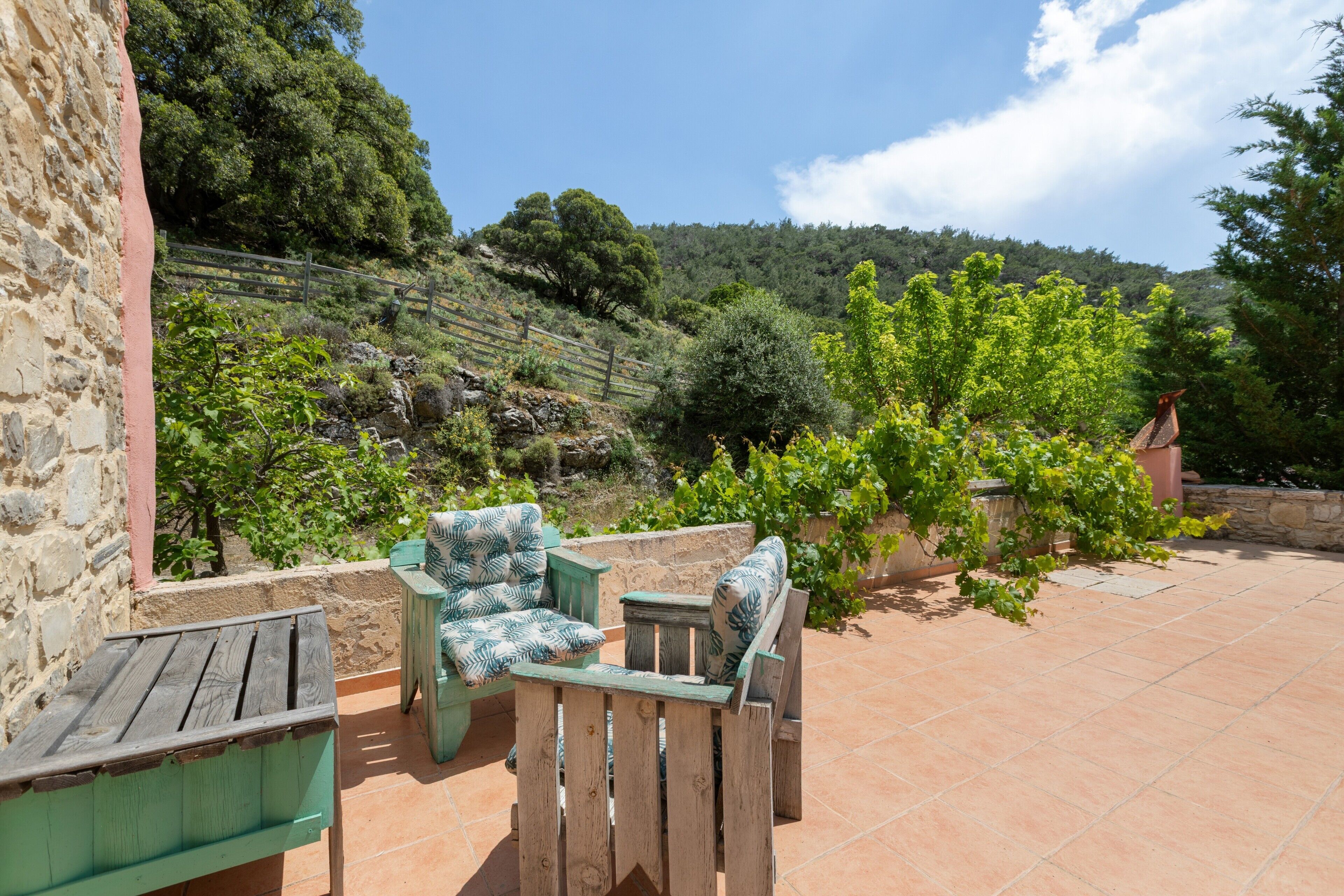 A patio with wooden furniture and a stone wall.