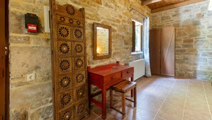 Una habitación con paredes de piedra, un armario de madera, un espejo y un banco.