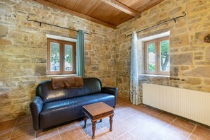 Une pièce aux murs de pierre, avec un canapé en cuir, une petite table en bois et un radiateur.