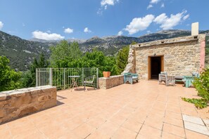 A stone building with a door, a small patio with a table and chairs, and a metal fence.
