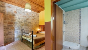 Un dormitorio con pared de piedra, techo de madera, cama, mesita de noche y otro velador.