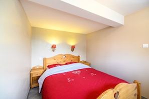 A bedroom with a wooden headboard, a red bedspread, two bedside lamps, and a nightstand. - Chalet 'La Sportive' with Mountain View, Private Garden and Wi-Fi (Cornimont)