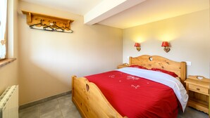 Un dormitorio con una cama de madera, un estante de madera con ganchos, dos lámparas de noche y un radiador.