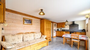 Una sala acogedora con un sofá de madera, una mesa de comedor con sillas, una cocina con armarios de madera y un aplique de techo.