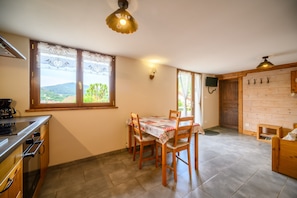 A kitchen with a dining table, chairs, a stove, and a window with a view of the outdoors. - Chalet 'La Sportive' with Mountain View, Private Garden and Wi-Fi (Cornimont)